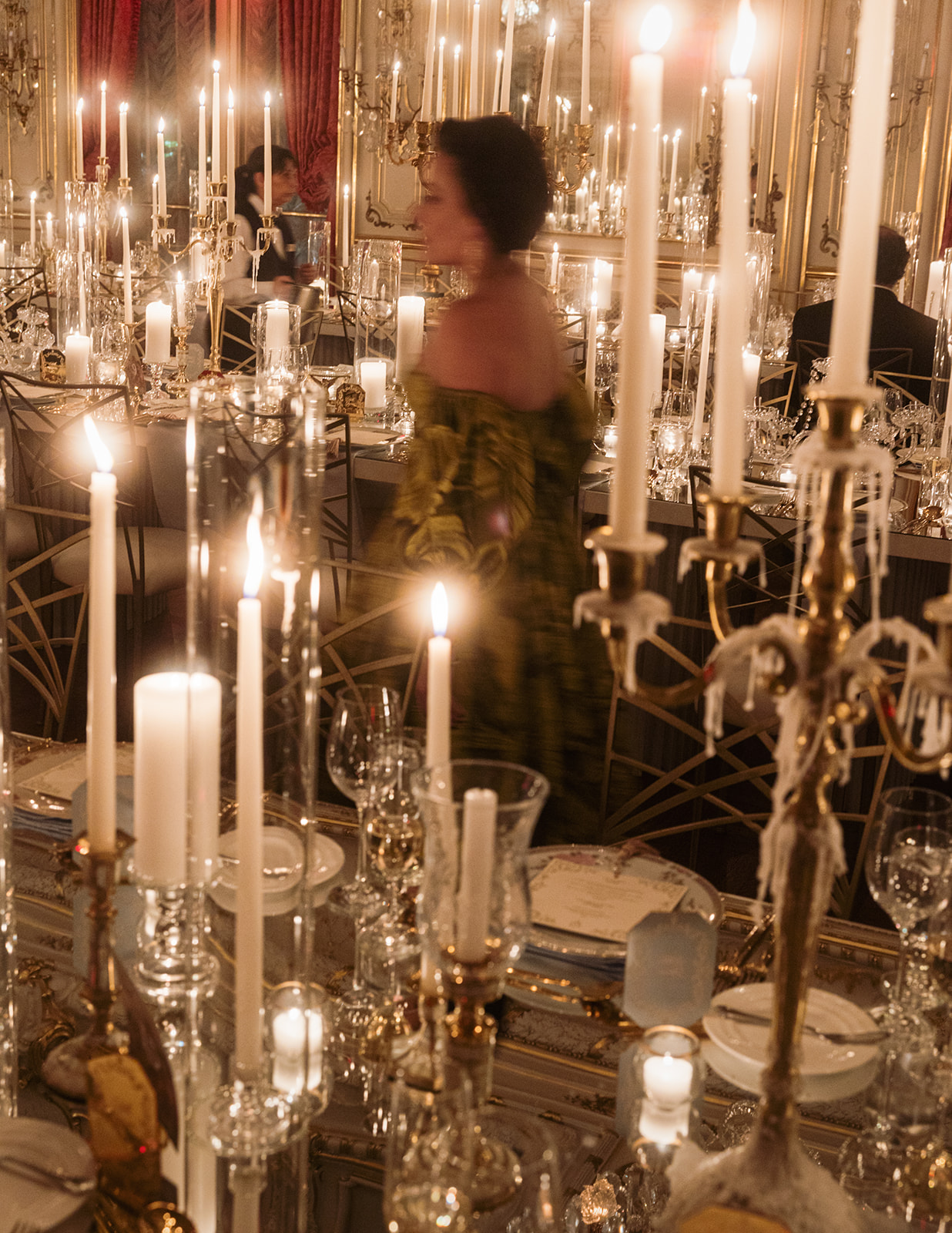 Close up of crystal candle holders and gold luxury wedding chairs with guests in a ballroom.