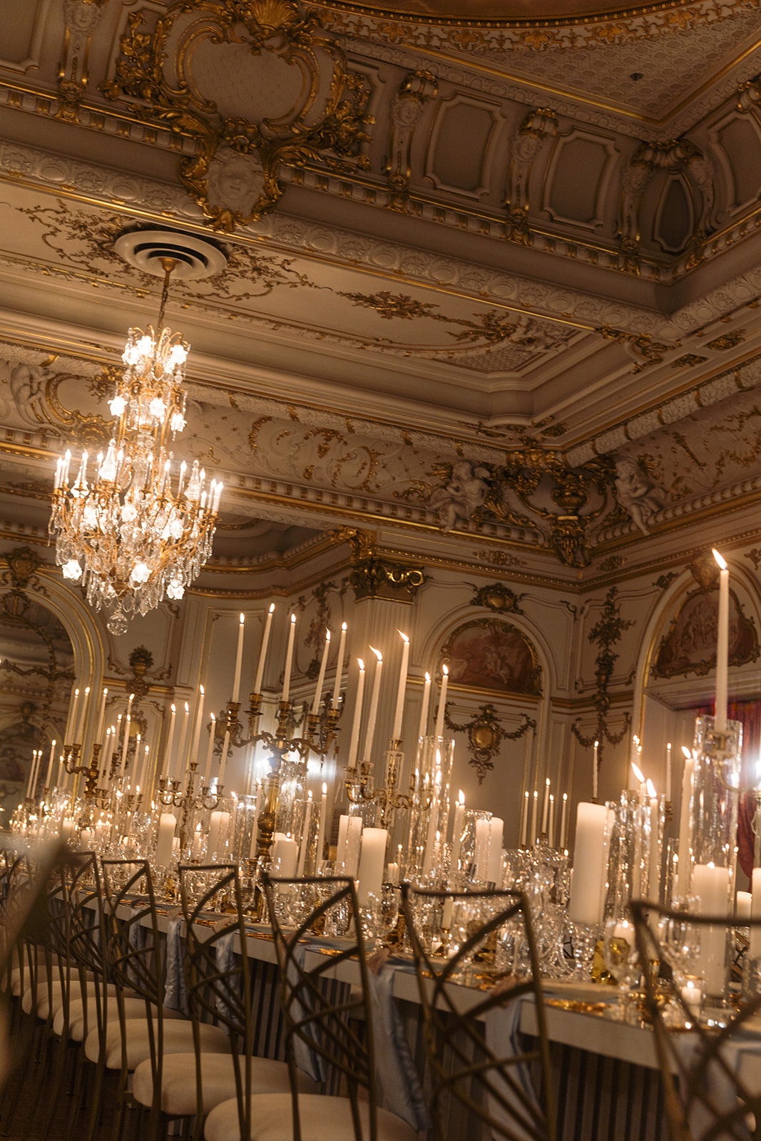 Looking up past rows of elegant guest seating toward a crystal chandelier and gilded ceiling moldings.